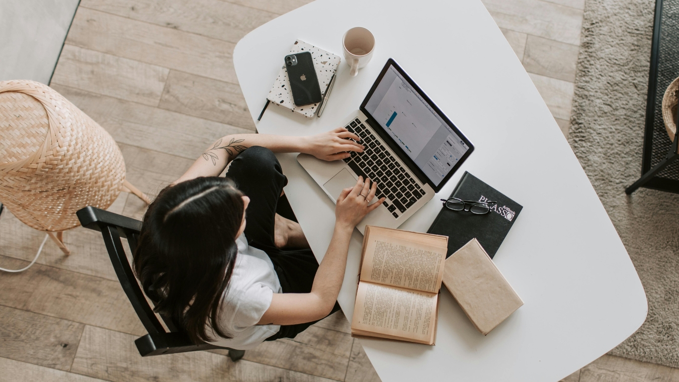 Frau arbeitet an einem Laptop, umgeben von Büchern und Notizen, während sie die deutschen Artikel und ihre Verwendung studiert.